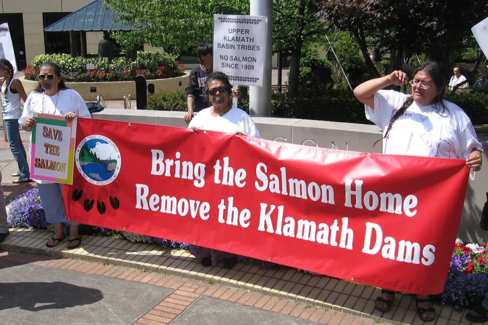Native demonstrators hold a red banner reading "Bring the salmon home - Remove the Klamath Dams."
